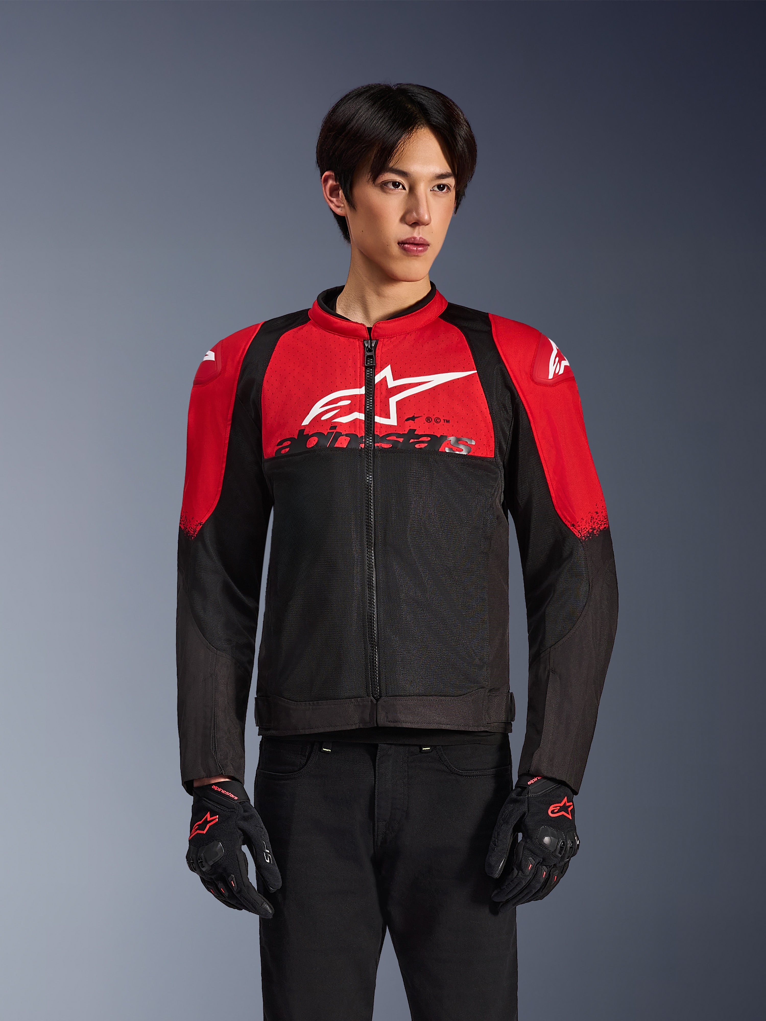 Giacca Alpinestars SMX Air, giacca da moto in rete, rosso acceso e nero, indossata da un modello con guanti da guida neri, con un grande logo bianco sul petto, costruzione in tessuto ventilato con pannelli rossi sulle spalle e maniche nere, abbigliamento sportivo performante per climi caldi