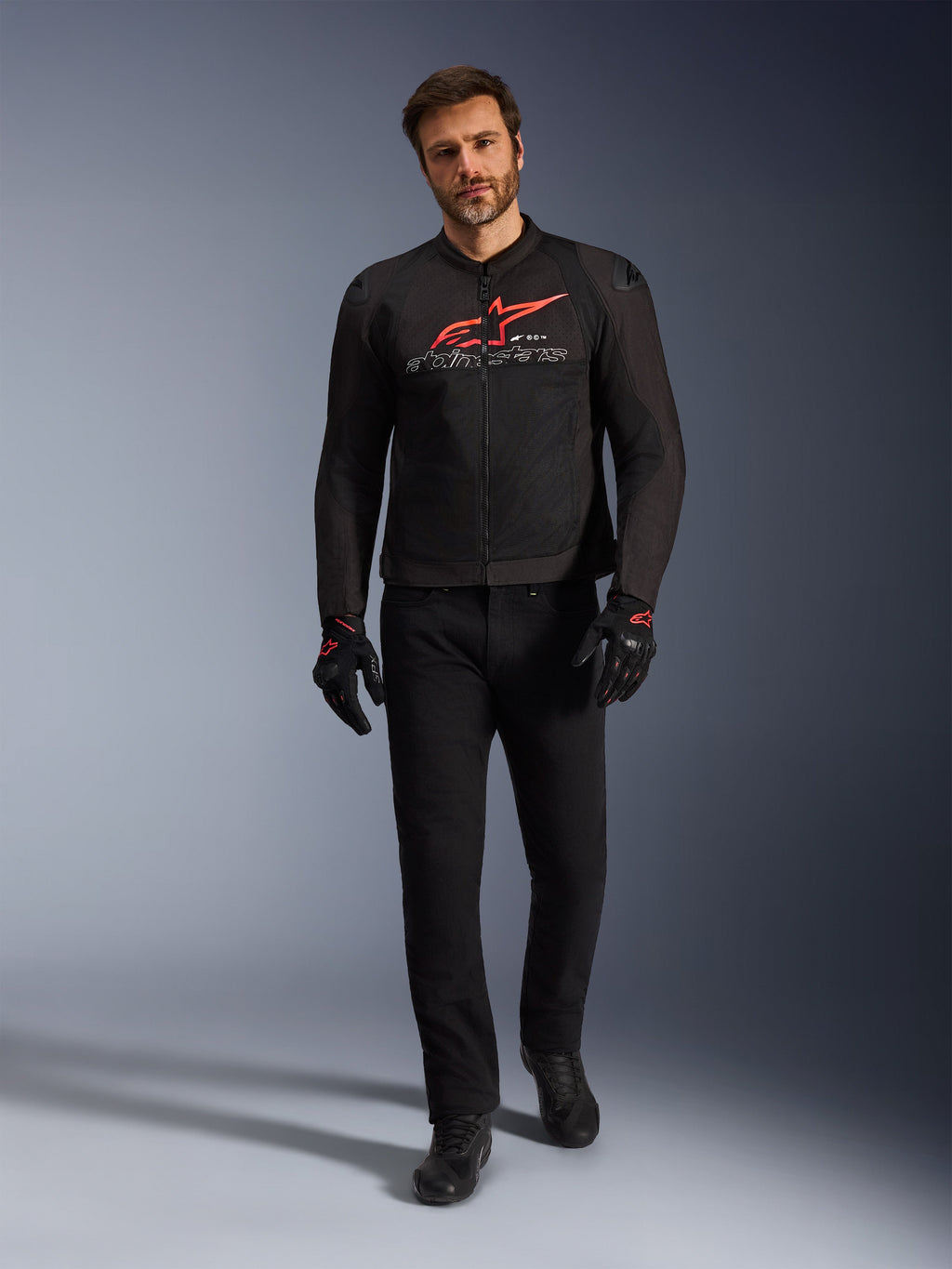 Giacca Alpinestars SMX Air, nero, rosso brillante e bianco, giacca da moto sportiva indossata con pantaloni da guida e guanti neri, con pannelli in rete tecnica e un vistoso logo Alpinestars rosso sul petto, outfit da strada ad alte prestazioni