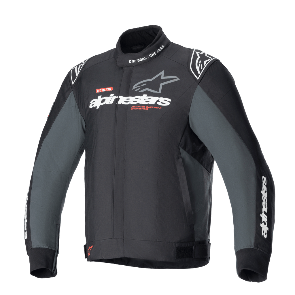 Giacca Alpinestars Monza Sport, giacca da moto in tessuto Black Tar Gray, colletto alto con scritta "ONE GOAL. ONE VISION.", loghi Alpinestars bianchi e grigi sul petto, loghi a stella sulle spalle, dettagli grafici rossi, linguette di regolazione in vita, design tecnico elegante