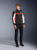 Giacca Alpinestars Monza Sport, nero, rosso acceso e bianco, giacca da moto in tessuto, design ispirato alle corse con marchio ASTARS su petto e maniche, indossata da un modello con pantaloni neri e scarpe da moto, abbigliamento da guida casual sportivo