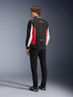 Giacca Alpinestars Monza Sport, giacca da moto in tessuto, nero, rosso brillante e bianco, vista posteriore del modello con pannelli laterali rossi e dettagli bianchi sulle maniche, logo Alpinestars e scritta 'ONE GOAL. ONE VISION.', abbinata a pantaloni neri e scarpe da guida per un look d'ispirazione sportiva.
