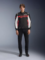 Modello che indossa la giacca Alpinestars Monza Sport in nero, rosso acceso e bianco, con un grande logo 'ASTARS' rosso sul petto e pannelli bianchi sulle maniche, abbinata a pantaloni neri e stivali da moto neri.