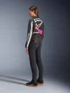 Giacca Alpinestars Idles da donna, giacca da moto, nero, bianco sporco e viola, vista dal retro su modella, con un grande logo Alpinestars avvolgente e design d'ispirazione racing vintage, abbinata a jeans scuri e scarpe nere.