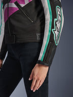 Giacca da donna Alpinestars Idles, vista ravvicinata della manica e del busto laterale, nera con dettagli viola, bianchi e verde acqua, con un audace logo Alpinestars sul braccio, polsino con zip e bottone a pressione e cinturino di regolazione in vita, abbigliamento da moto d'ispirazione vintage.