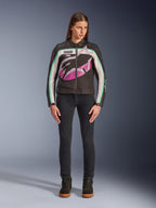 Donna che indossa la giacca Alpinestars Idles Donna, nero, bianco sporco e viola, design di ispirazione racing vintage con grande logo avvolgente e accenti verde acqua, abbinata a jeans neri e sneakers da moto, abbigliamento motociclistico urbano