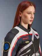Giacca da donna Alpinestars Idles, bianco panna, rosso fiamma e nero, con toppe da corsa d'ispirazione vintage e logo avvolgente, struttura in tessuto e pelle, stile motociclistico urbano indossata da una modella