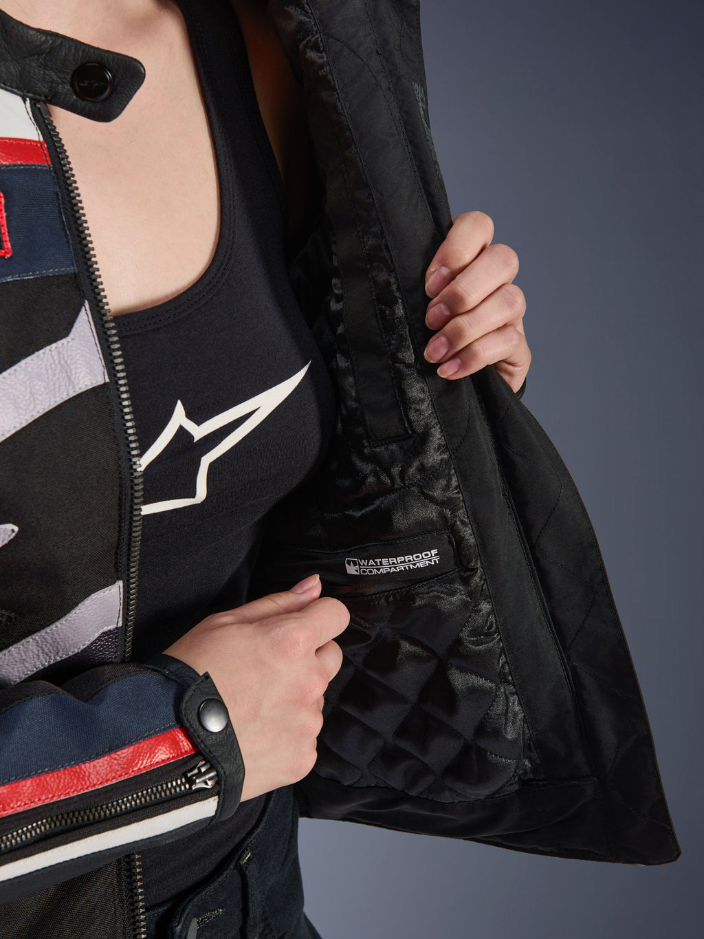 Giacca da donna Alpinestars Idles, dettaglio interno con fodera nera trapuntata e scomparto impermeabile con etichetta, indossata sopra una canotta nera con logo, abbigliamento tecnico da moto per donna