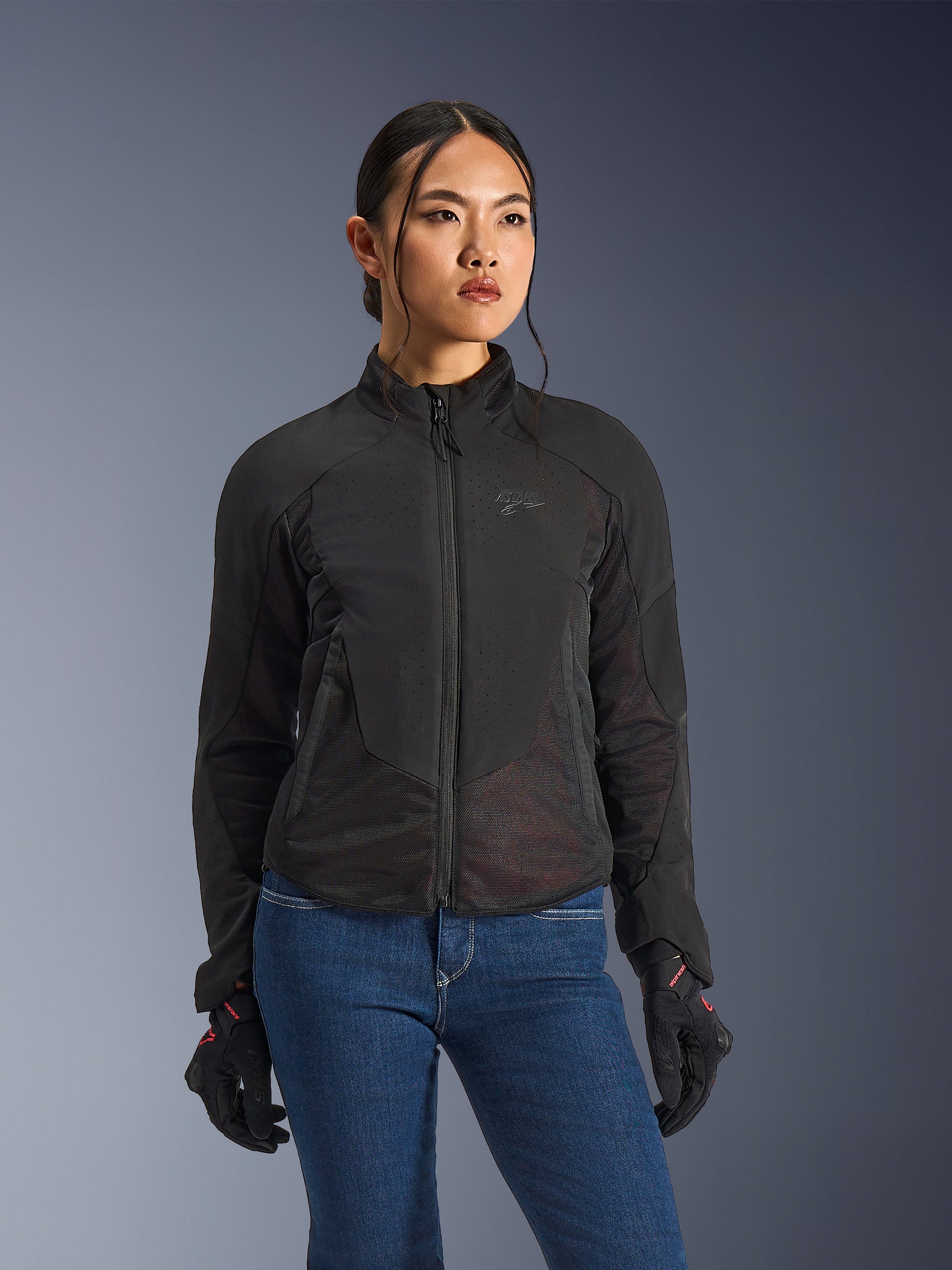 Alpinestars Stella Aeroshell Airflow Jacket da donna, giacca moto nera con perforazioni, colletto alto e zip frontale, indossata con guanti neri e jeans blu