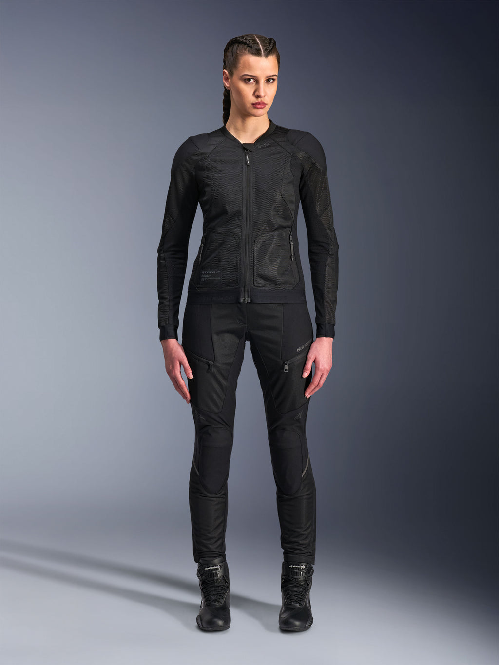 Giacca Alpinestars Stella Troop-Air, giacca da moto da donna, nera, costruzione in mesh tecnico 2D dal design minimalista, indossata con pantaloni da moto e stivali neri, stile motociclistico urbano contemporaneo.