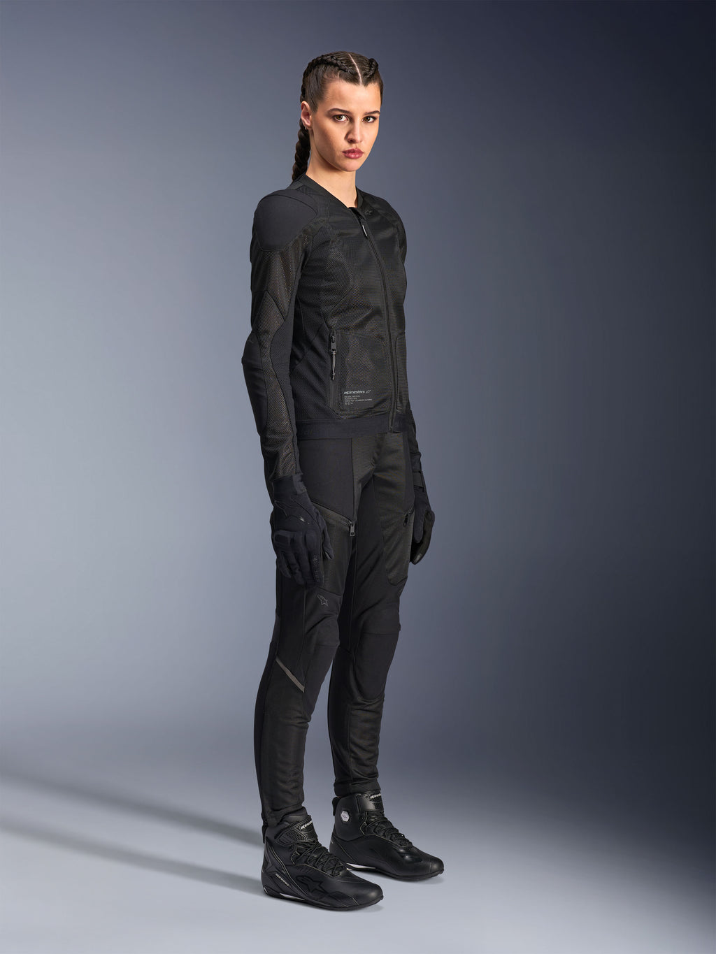 Motociclista donna che indossa la giacca Alpinestars Stella Troop-Air in nero, caratterizzata da una costruzione in mesh tecnico 2D, abbinata a pantaloni, guanti e stivali da moto neri coordinati, in stile urban riding.
