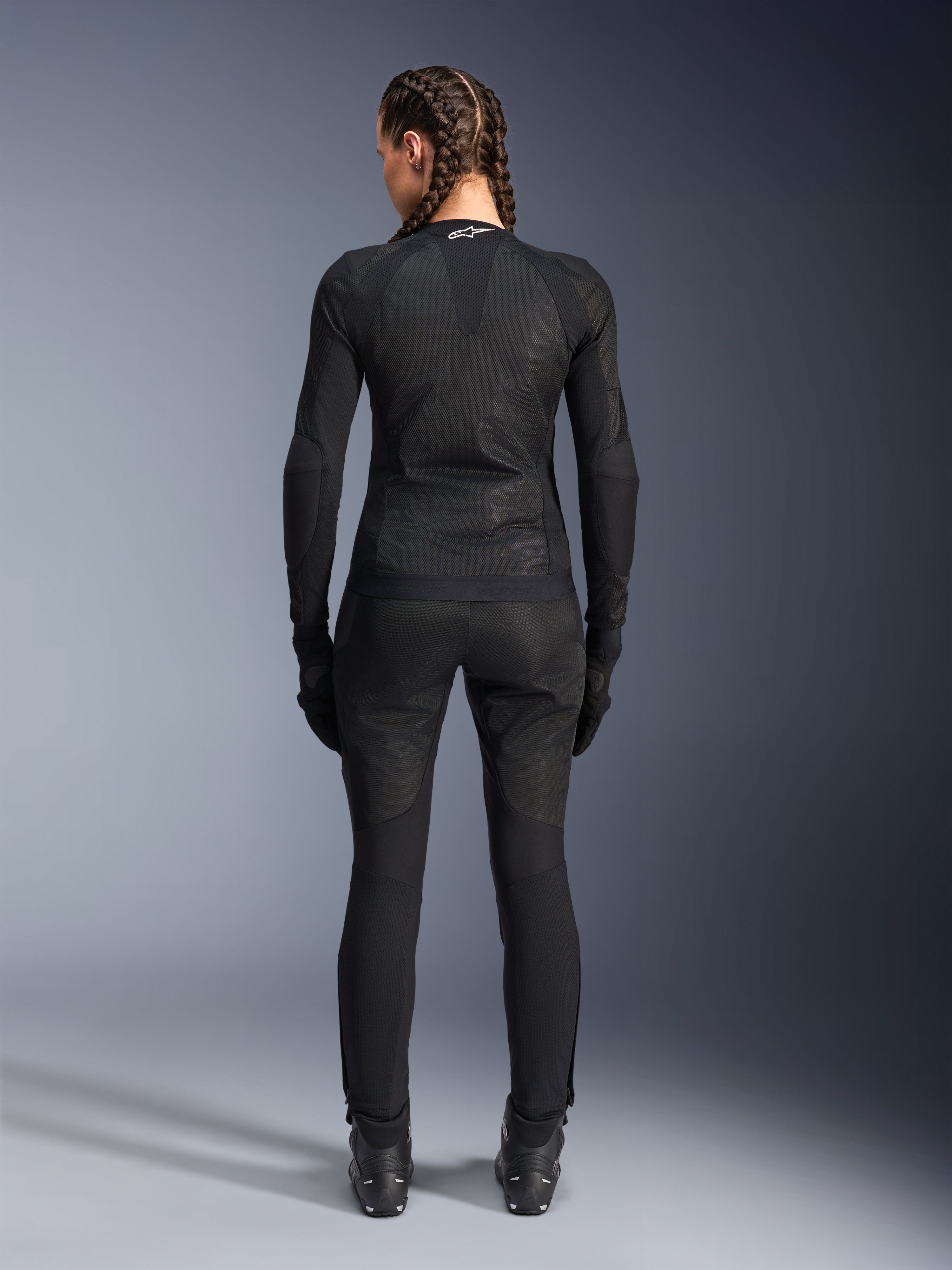 Giacca Alpinestars Stella Troop-Air, giacca da moto da donna, nera, vista posteriore di una motociclista che indossa una giacca in mesh tecnico, abbinata a pantaloni da moto, guanti e stivali neri coordinati, design traspirante e aderente con logo Alpinestars bianco sul colletto