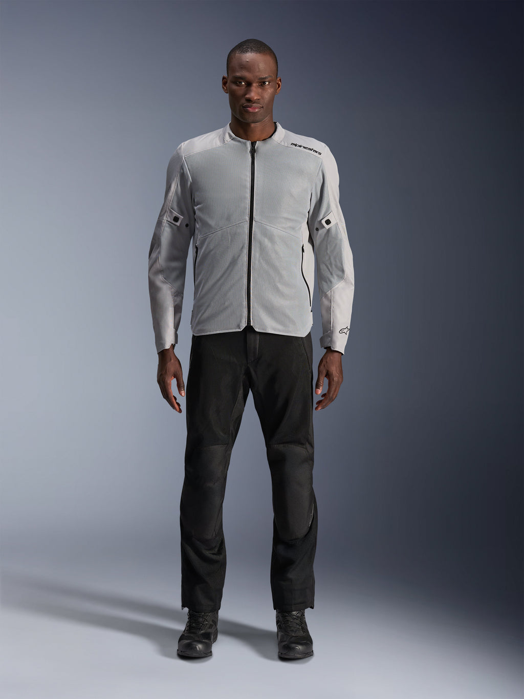 Giacca Alpinestars C-1 Air in Silver, giacca da moto urban in tessuto da uomo con pannelli in rete ventilata, indossata da un modello con pantaloni da guida neri e stivali neri, stile commuting contemporaneo