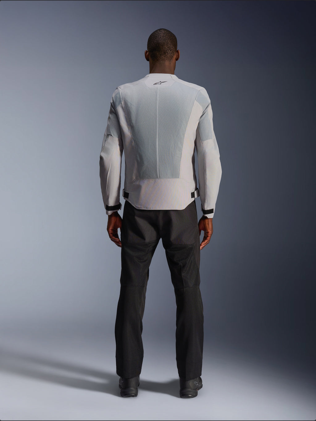 Giacca Alpinestars C-1 Air in Silver, vista dal retro su un modello maschile, giacca da moto in tessuto con ampi pannelli di ventilazione in mesh tecnico, piccolo logo nero sul collo e regolatori in vita, indossata con pantaloni da guida neri per un look urban contemporary.