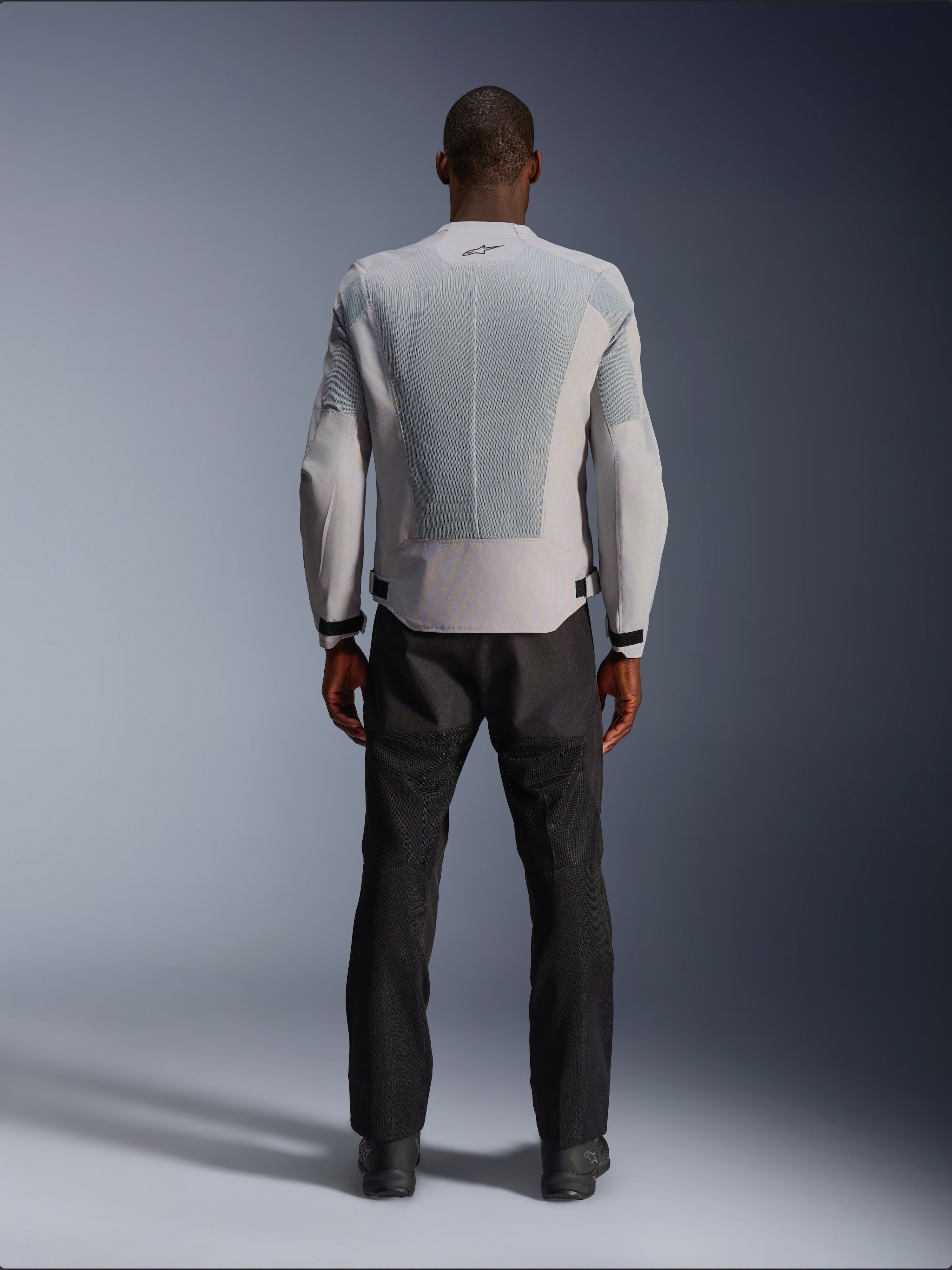 Giacca Alpinestars C-1 Air in Silver, vista dal retro su un modello maschile, giacca da moto in tessuto con ampi pannelli di ventilazione in mesh tecnico, piccolo logo nero sul collo e regolatori in vita, indossata con pantaloni da guida neri per un look urban contemporary.