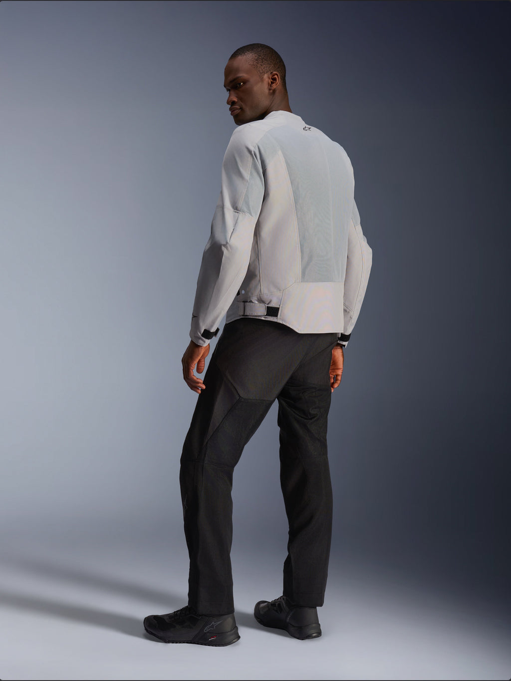 Giacca Alpinestars C-1 Air, argento e grigio, vista dal retro su un modello, con pannelli in mesh tecnico ventilato e loghi riflettenti, indossata con pantaloni e scarpe neri, abbigliamento da moto urban contemporary.