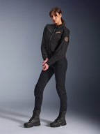 Modella che indossa la Giacca Alpinestars Stella Grace, giacca da moto urbana nera, abbinata a pantaloni da guida e stivali neri, design d'ispirazione workwear con logo ricamato color bronzo sul petto e patch circolare a spirale sulla manica
