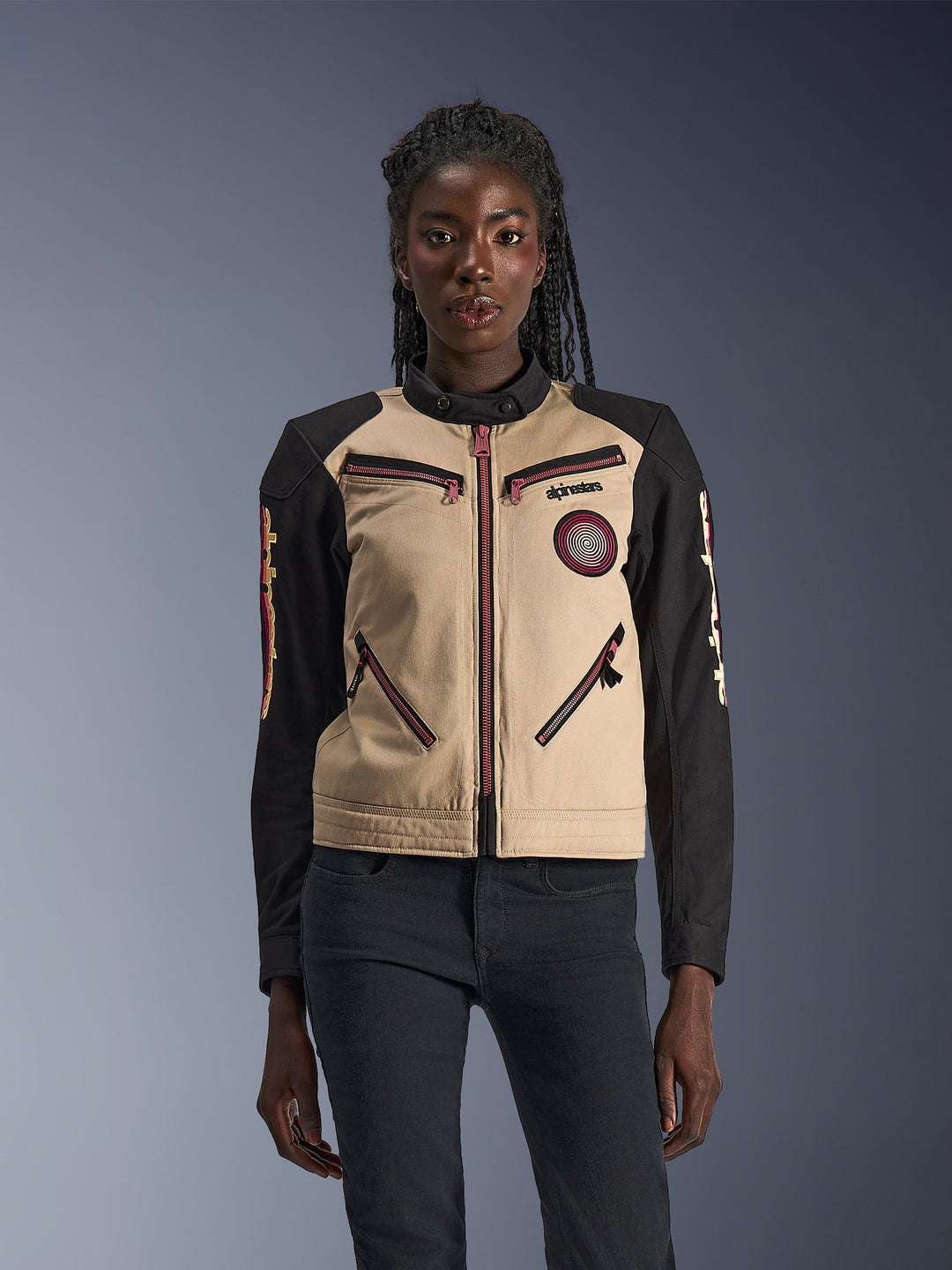 Giacca Alpinestars Stella Grace, giacca da moto da donna, color alluminio e nero, caratterizzata da un design ispirato al workwear con dettagli delle zip rosso-rosa, una patch a spirale sul petto e maniche lunghe nere con grafiche gialle e rosse, indossata da una modella.