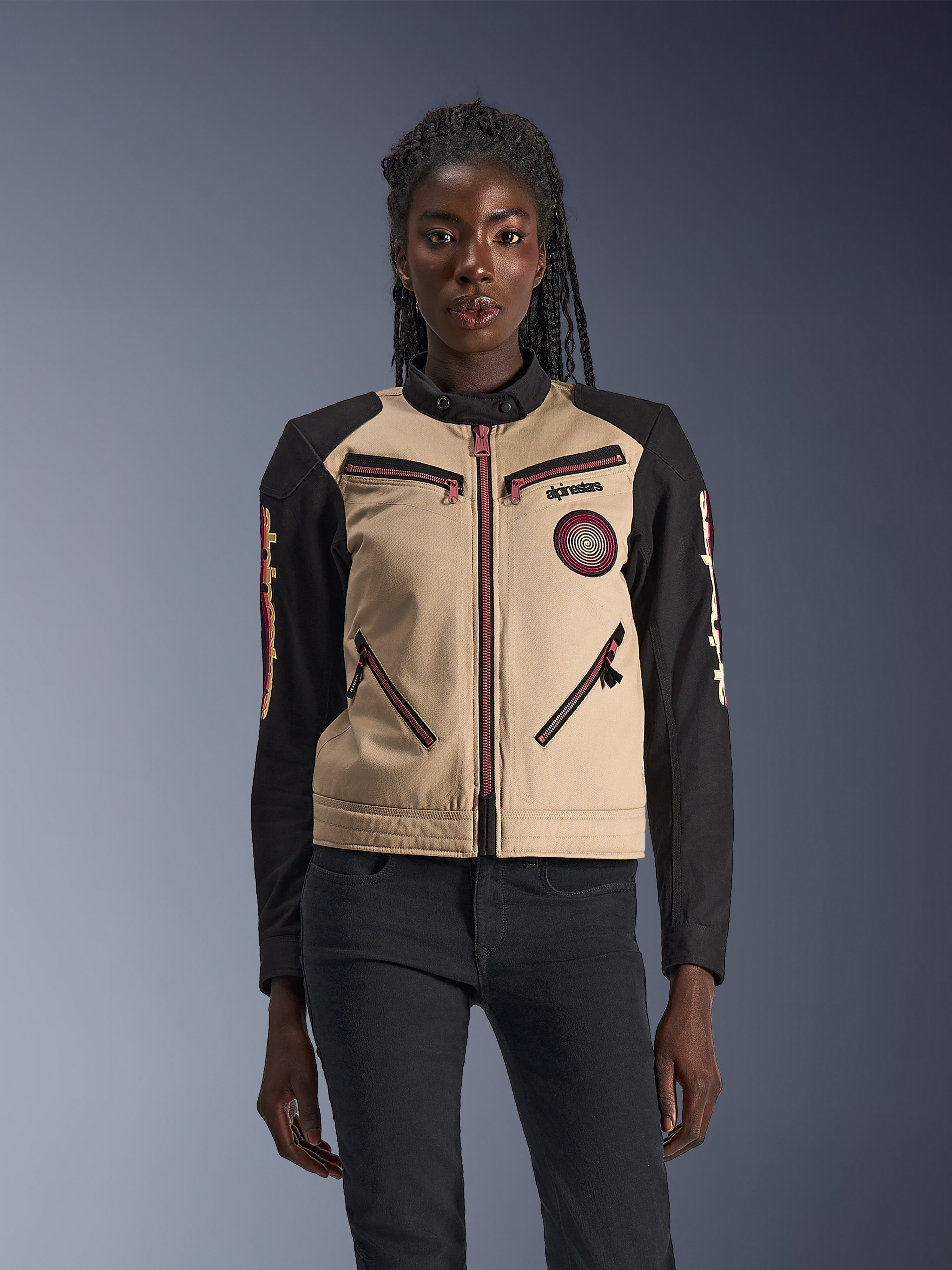 Giacca Alpinestars Stella Grace, giacca da moto da donna, color alluminio e nero, caratterizzata da un design ispirato al workwear con dettagli delle zip rosso-rosa, una patch a spirale sul petto e maniche lunghe nere con grafiche gialle e rosse, indossata da una modella.