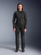 Donna che indossa la giacca Alpinestars Stella C-1 Air in nero, abbinata a pantaloni da moto in tessuto nero coordinati e scarpe da guida, caratterizzata da un design urbano elegante con ampi pannelli in mesh per il flusso d'aria.
