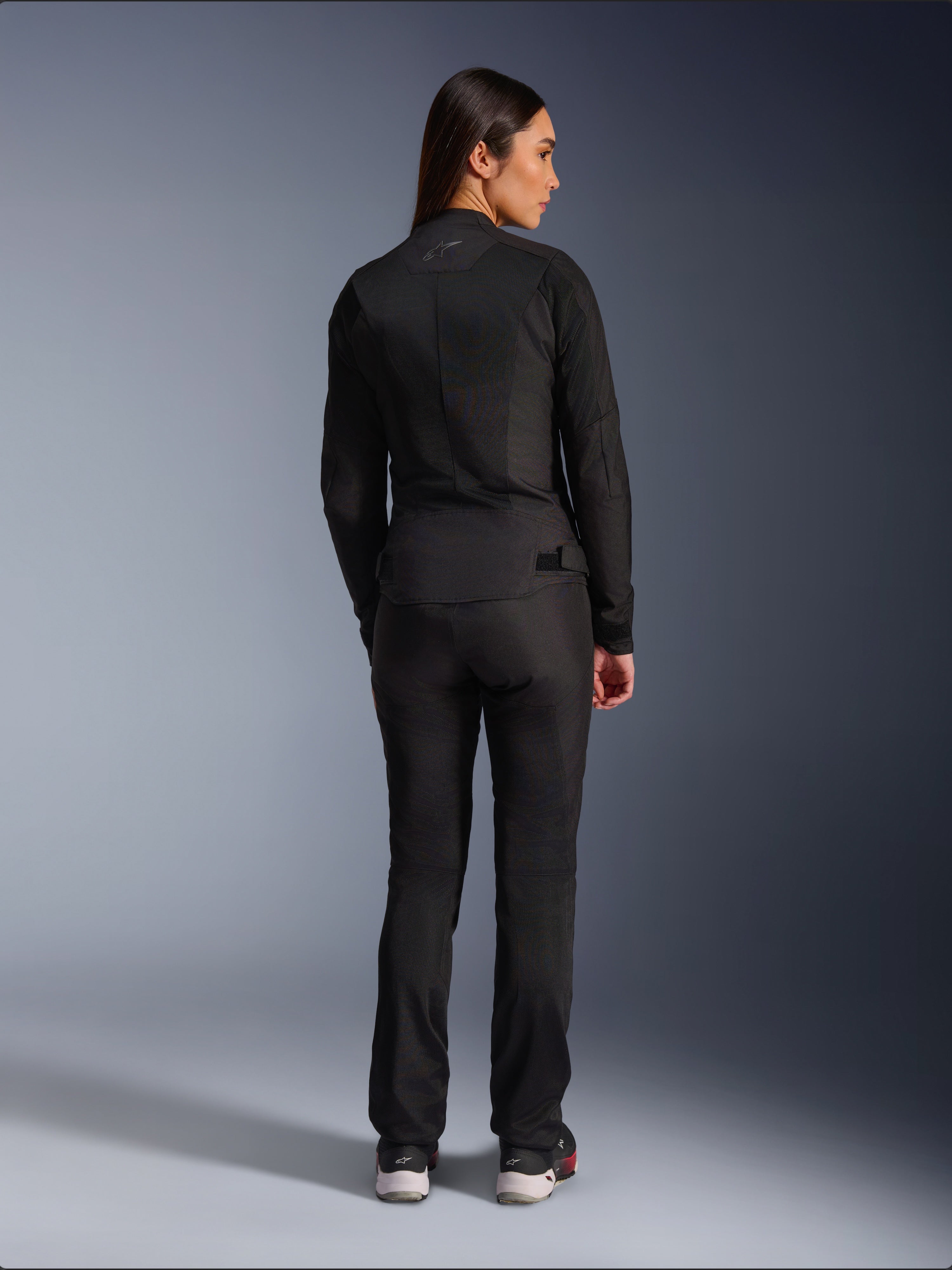 Giacca Alpinestars Stella C-1 Air, giacca da moto in tessuto per donna, nera, vista posteriore che mostra la costruzione in mesh e il logo discreto sulla parte superiore della schiena, indossata con pantaloni da moto neri coordinati, stile urban contemporaneo.