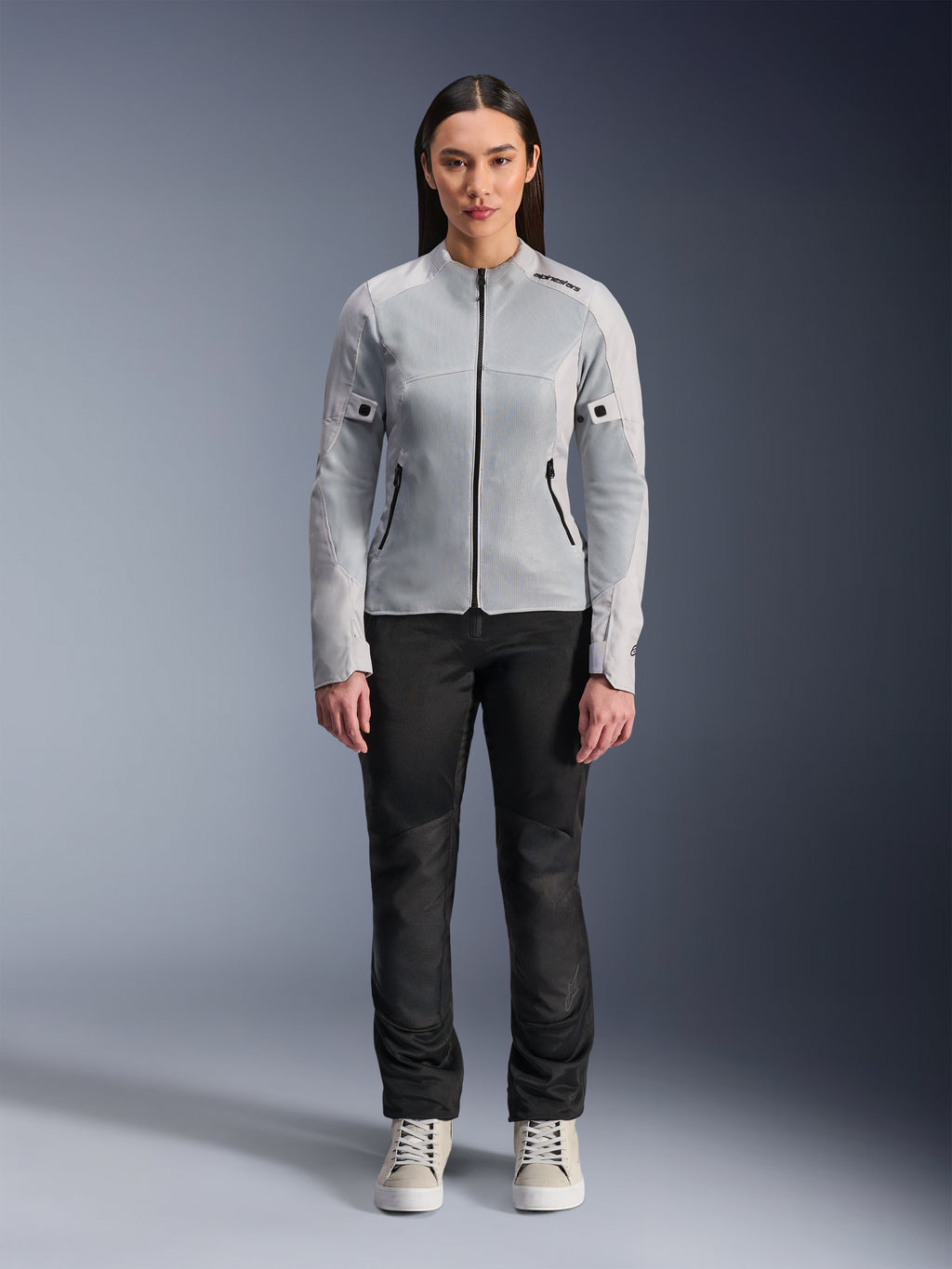 Donna che indossa la giacca Alpinestars Stella C-1 Air in Silver, vista frontale, giacca da moto urbana in tessuto con pannelli in rete tecnica, abbinata a pantaloni neri e sneakers bianche, abbigliamento da moto contemporaneo