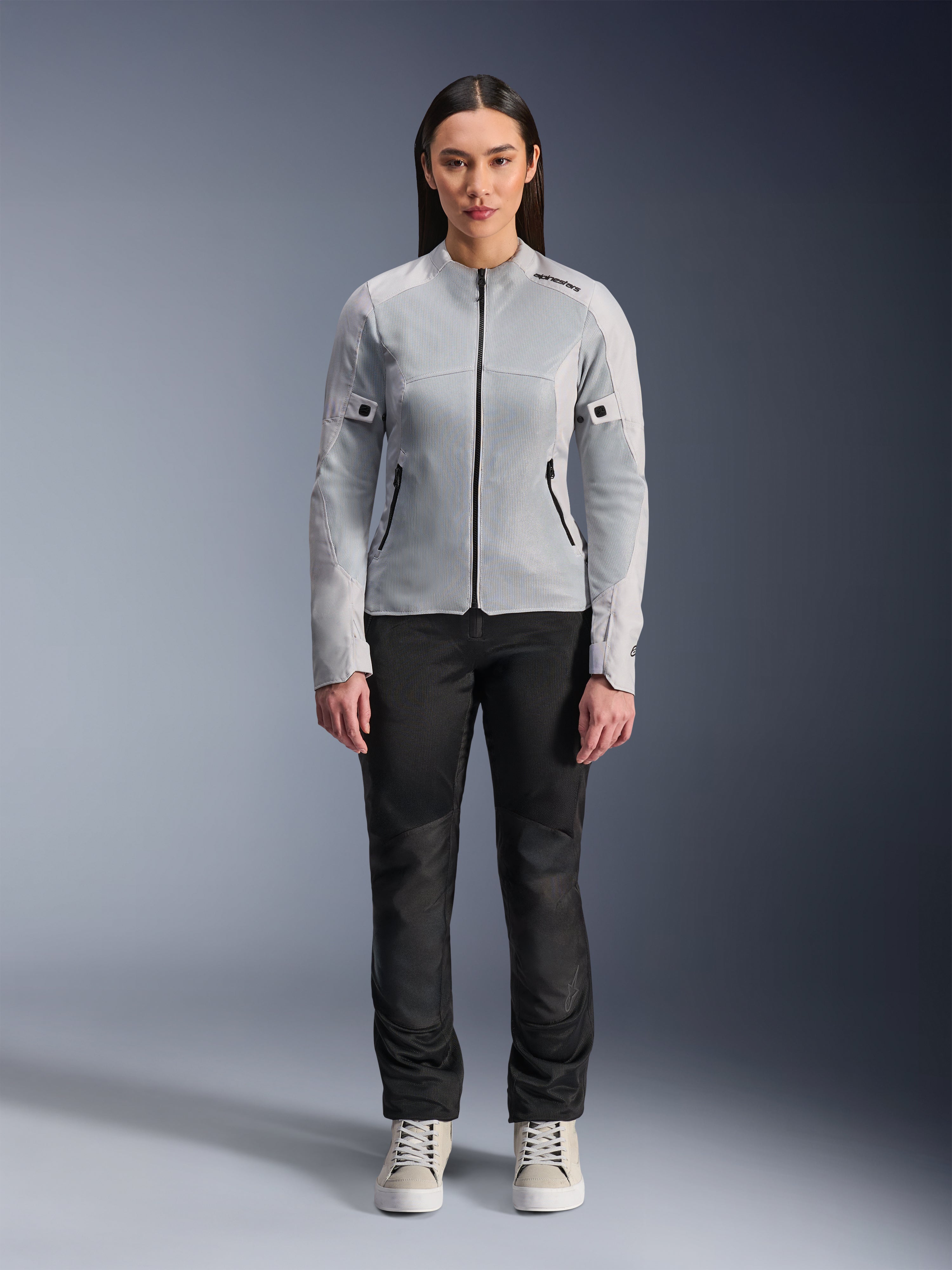 Donna che indossa la giacca Alpinestars Stella C-1 Air in Silver, vista frontale, giacca da moto urbana in tessuto con pannelli in rete tecnica, abbinata a pantaloni neri e sneakers bianche, abbigliamento da moto contemporaneo
