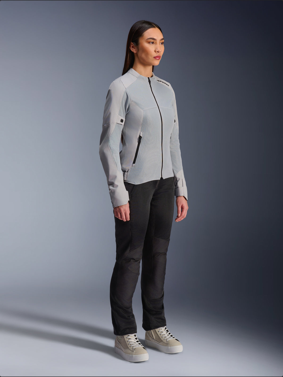 Donna che indossa la giacca Alpinestars Stella C-1 Air in Silver, giacca da moto leggera in tessuto e mesh, abbinata a pantaloni da moto neri e sneaker casual, estetica urban riding pulita.
