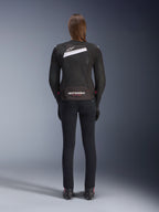 Giacca Alpinestars Stella T-GP Plus R V4 Airflow, nero e bianco, vista posteriore con ampi pannelli di ventilazione in mesh e marchio Alpinestars, indossata da una pilota con pantaloni da moto neri slim-fit e stivali, abbigliamento tecnico sportivo in tessuto da donna