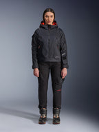 Modella che indossa la giacca Alpinestars Molly Air in nero e corallo fluo, caratterizzata da un design d'ispirazione utility con cappuccio e fodera interna corallo, abbinata a pantaloni da guida neri e stivali da moto, abbigliamento da moto urban contemporary