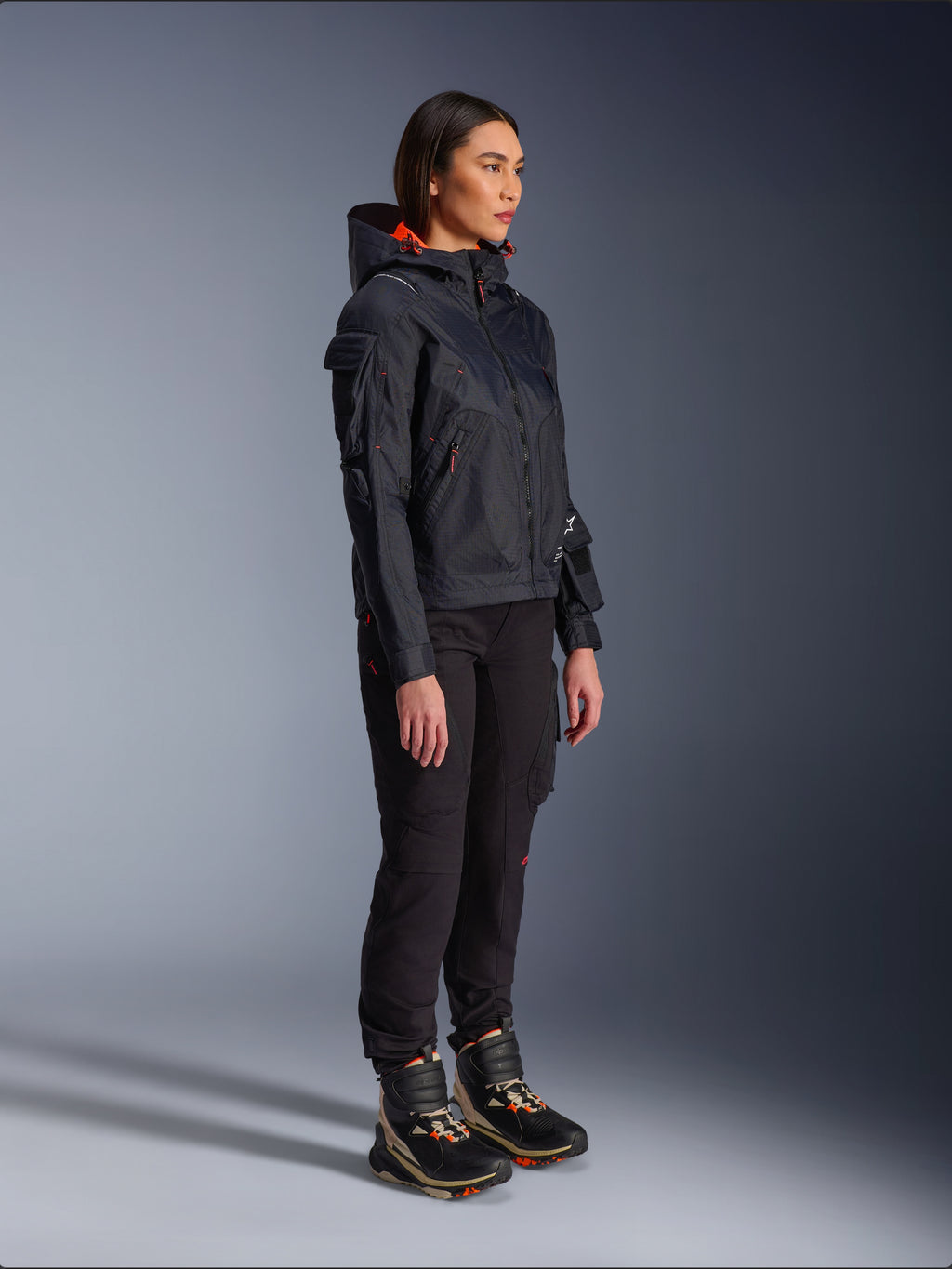 Alpinestars Pantaloni Actea da Donna in nero, vestibilità regolare con tasche cargo, abbinati a una giacca Molly Air nera con dettagli arancioni e scarpe da moto alte, abbigliamento motociclistico urbano contemporaneo per donna