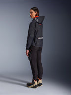 Motociclista donna che indossa la giacca Alpinestars Molly Air in Black Fluo Coral, vista laterale posteriore che mostra il cappuccio con logo Astars e grande marchio Alpinestars sulla schiena, abbinata a pantaloni cargo da moto neri e stivali adventure sabbia e neri, abbigliamento da moto urbano contemporaneo da donna