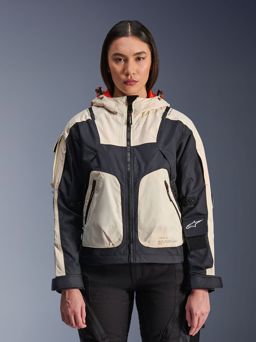 Alpinestars Molly Air Jacket, giacca da moto urban da donna, Black Almond, vista frontale su una modella, con pannelli in ripstop crema e nero, cappuccio con fodera arancione, chiusura frontale con cerniera e grandi tasche utility, abbigliamento da moto contemporaneo ispirato allo streetwear