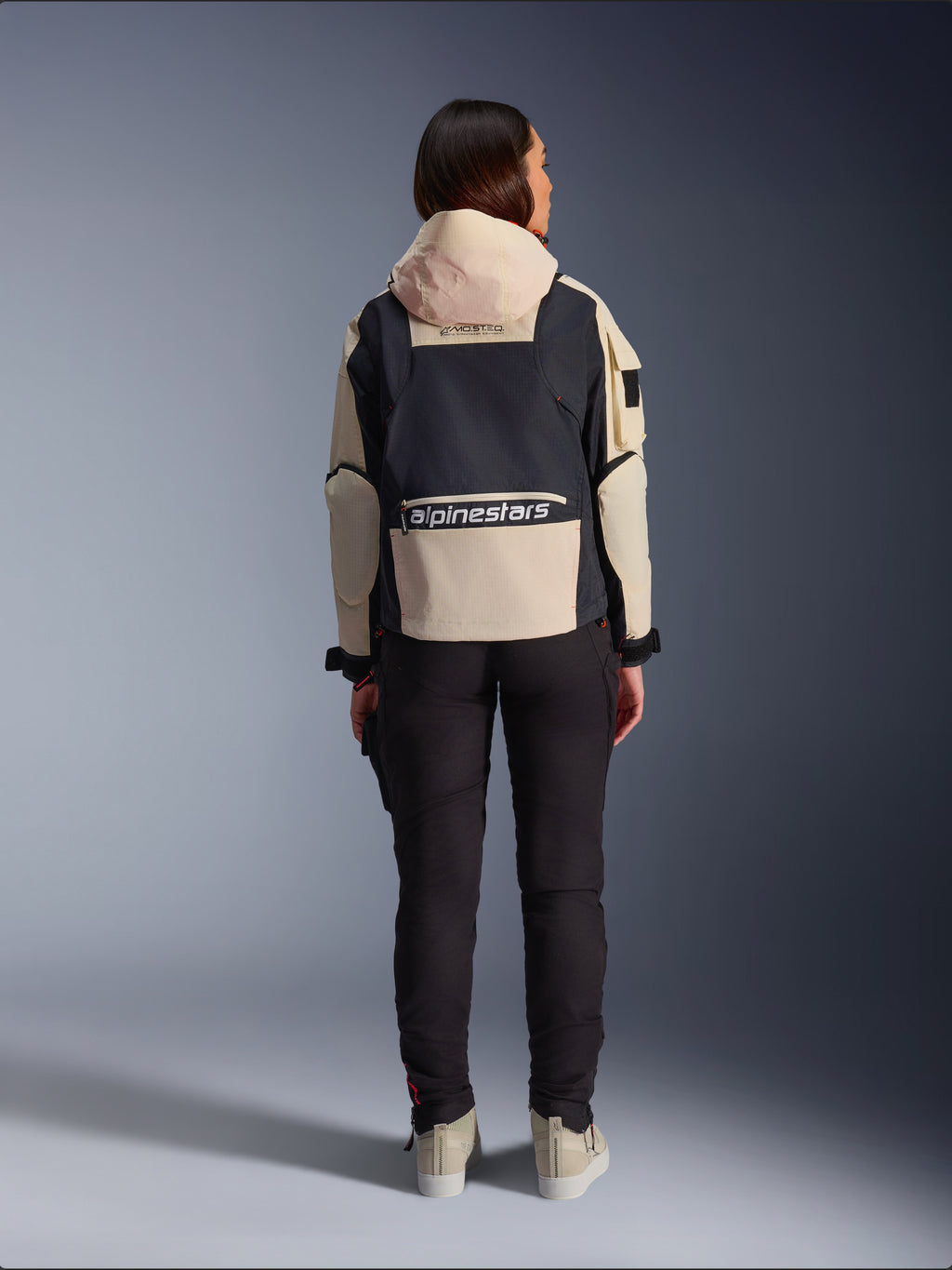 Giacca Alpinestars Molly Air, giacca da moto da donna, Black Almond, vista posteriore che mostra il cappuccio e il grande logo sulla schiena, design ripstop d'ispirazione utility, abbinata a pantaloni da moto neri.