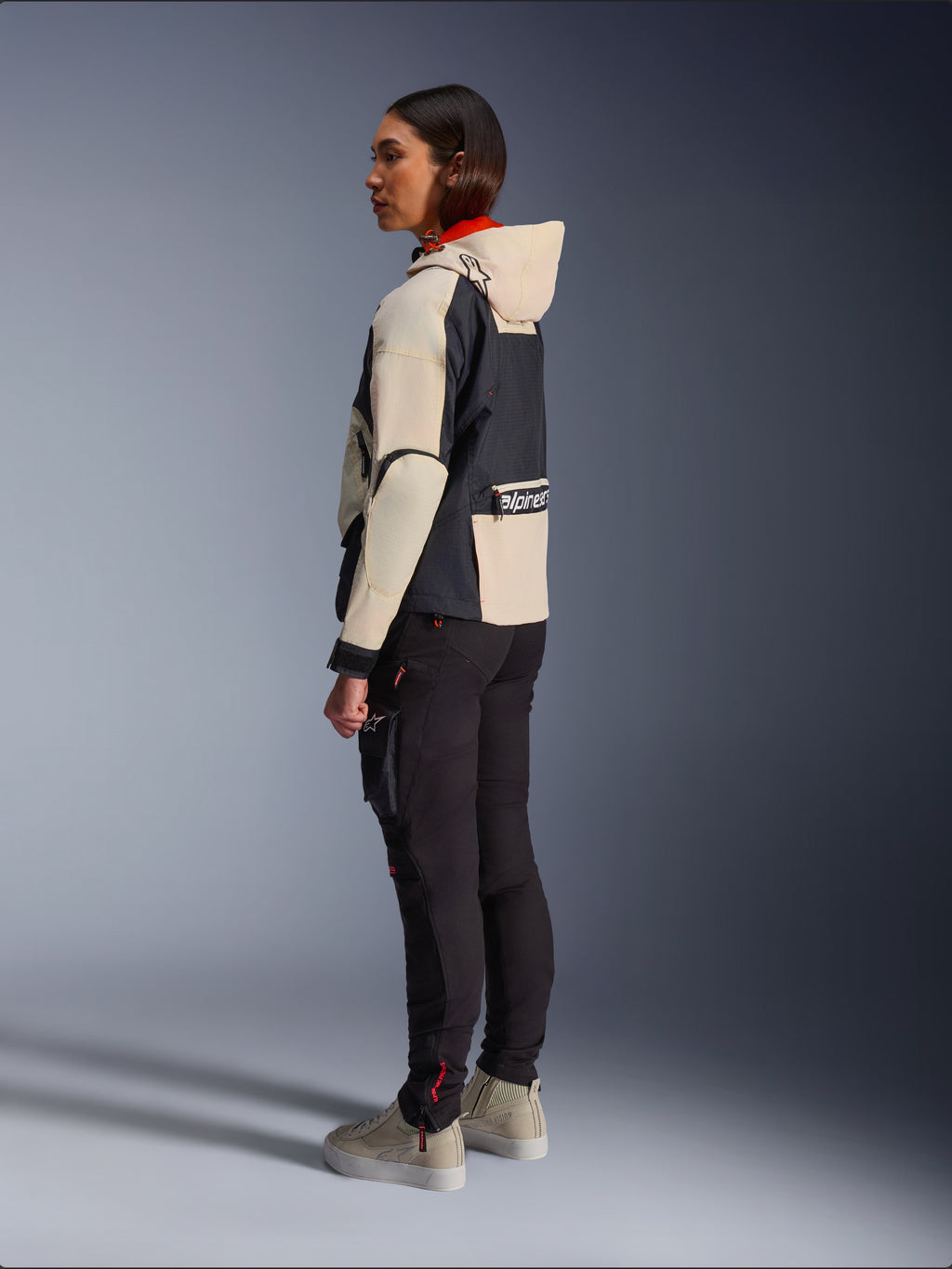 Giacca Alpinestars Molly Air, giacca da moto da donna, Black Almond, con design con cappuccio, maniche crema e busto nero, indossata con pantaloni da moto neri e sneakers beige, stile urban contemporaneo.
