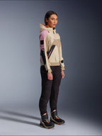 Modella che indossa la giacca Alpinestars Molly Air in Sand Pink Almond, abbinata a pantaloni tecnici scuri e stivali da moto alti, giacca da moto urbana con cappuccio e pannelli multicolore, design contemporaneo ispirato allo streetwear