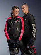 Giacca Alpinestars Stella T-Dyno Air su donna in nero, rosso brillante e fucsia, abbinata alla giacca da uomo Dyno Air nera, entrambi i motociclisti con caschi da moto in mano, scatto in studio di abbigliamento moto urban contemporary