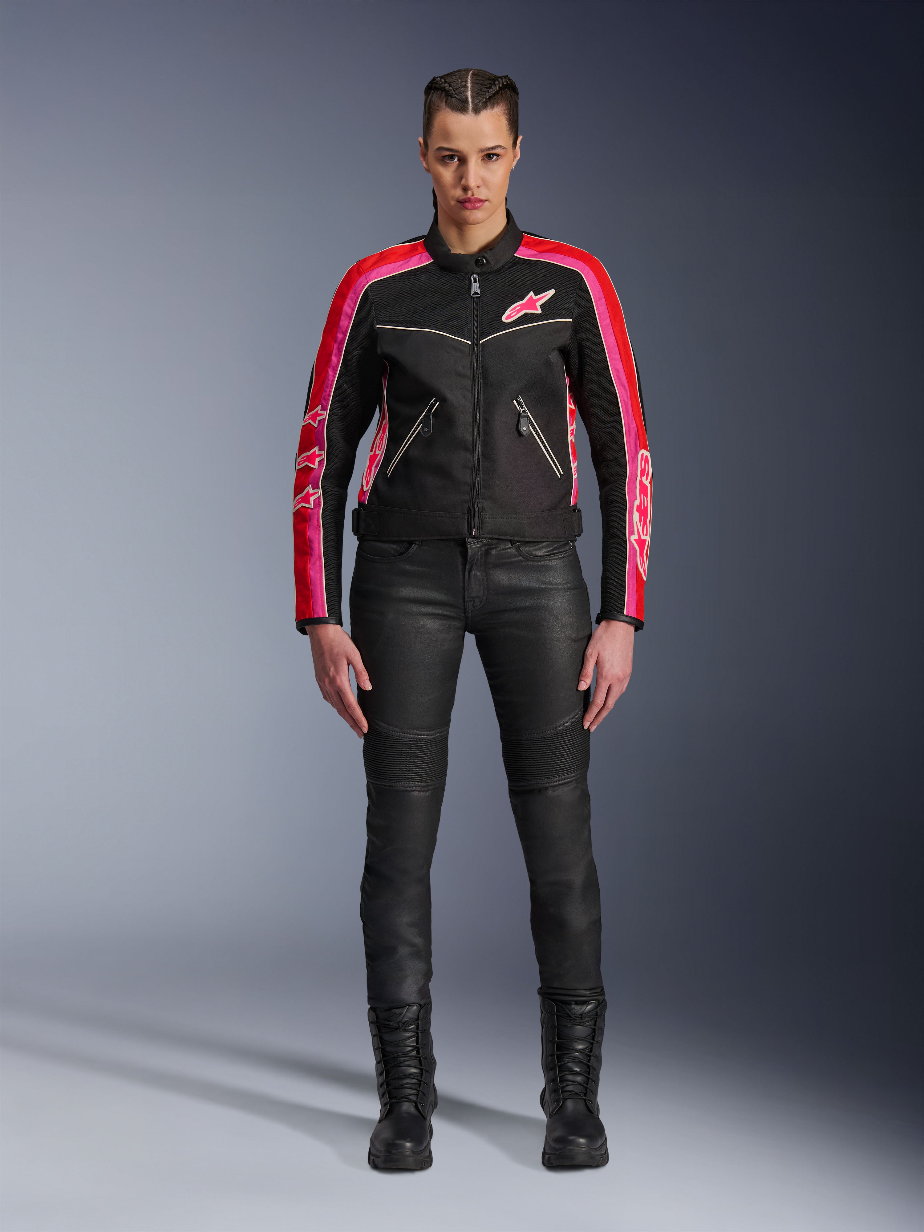 Motociclista che indossa la giacca Alpinestars Stella T-Dyno Air, nera con accenti rosso brillante e fucsia, abbinata a pantaloni da moto neri e stivali stringati, con pannelli in rete 3D, vestibilità su misura e loghi a stella rosa, abbigliamento da moto urban