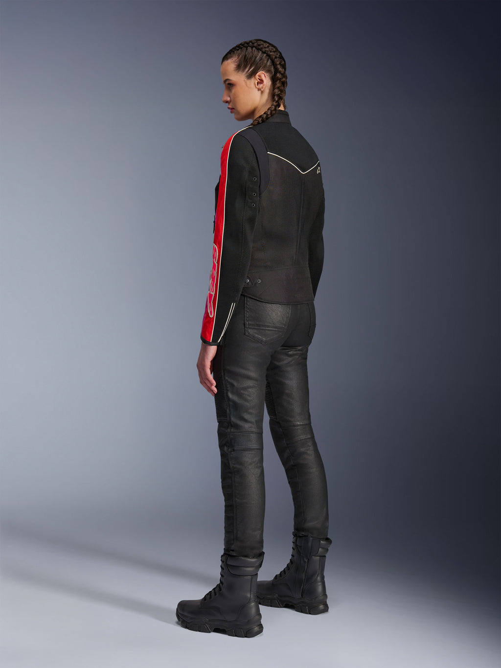 Donna che indossa la giacca Alpinestars Stella T-Dyno Air in Nero Rosso Brillante Fucsia, abbinata a pantaloni da moto neri e stivali neri, vista di profilo che mette in risalto le grafiche rosse e fucsia sulle maniche e la vestibilità da moto su misura.