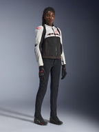 Giacca Alpinestars Stella SMX Air da donna in grigio ghiaccio, nero e corallo fluo, indossata da una modella con pantaloni da moto e guanti neri, caratterizzata da struttura in rete e loghi rosso corallo, abbigliamento tecnico sportivo da donna