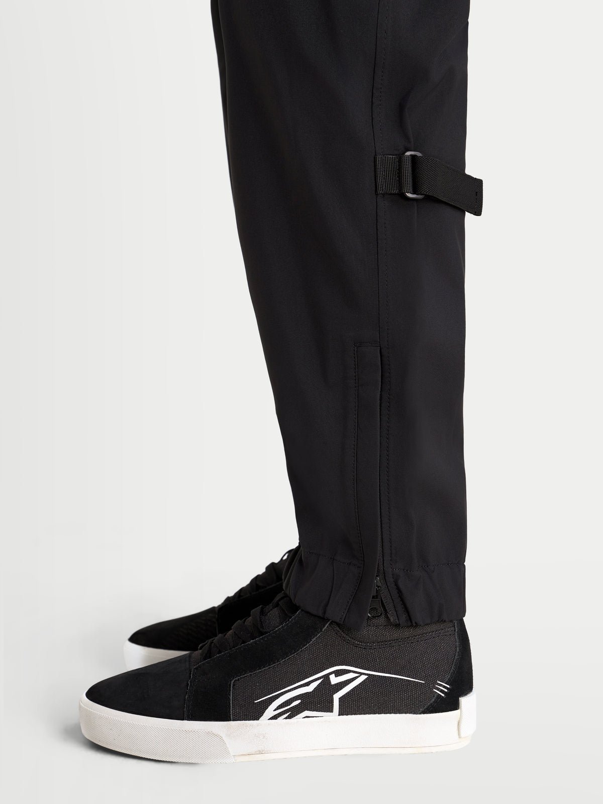 Alpinestars Juggernaut V 2 Drystar Pantaloni, pantaloni da moto urban impermeabili da uomo, colore nero, vista laterale ravvicinata che mostra la regolazione della parte inferiore della gamba e l'orlo elasticizzato con apertura con cerniera indossati da un modello