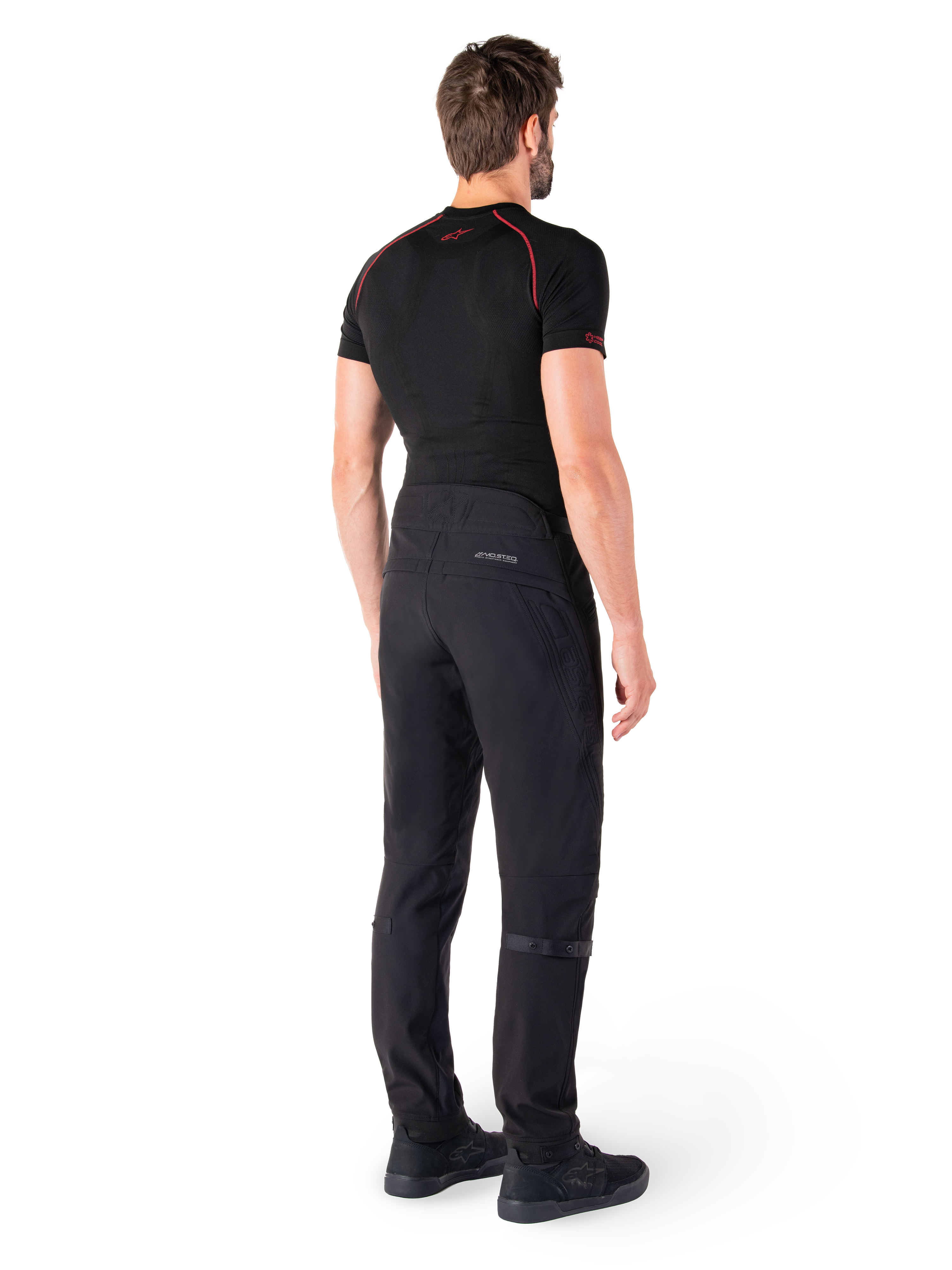Alpinestars Alden Pants, Nero, pantaloni da moto urban visti dal retro su un modello, indossati con un base layer nero a maniche corte e scarpe da guida nere, caratterizzati da dettagli trapuntati e marchio MO.ST.EQ. riflettente sul carré posteriore.