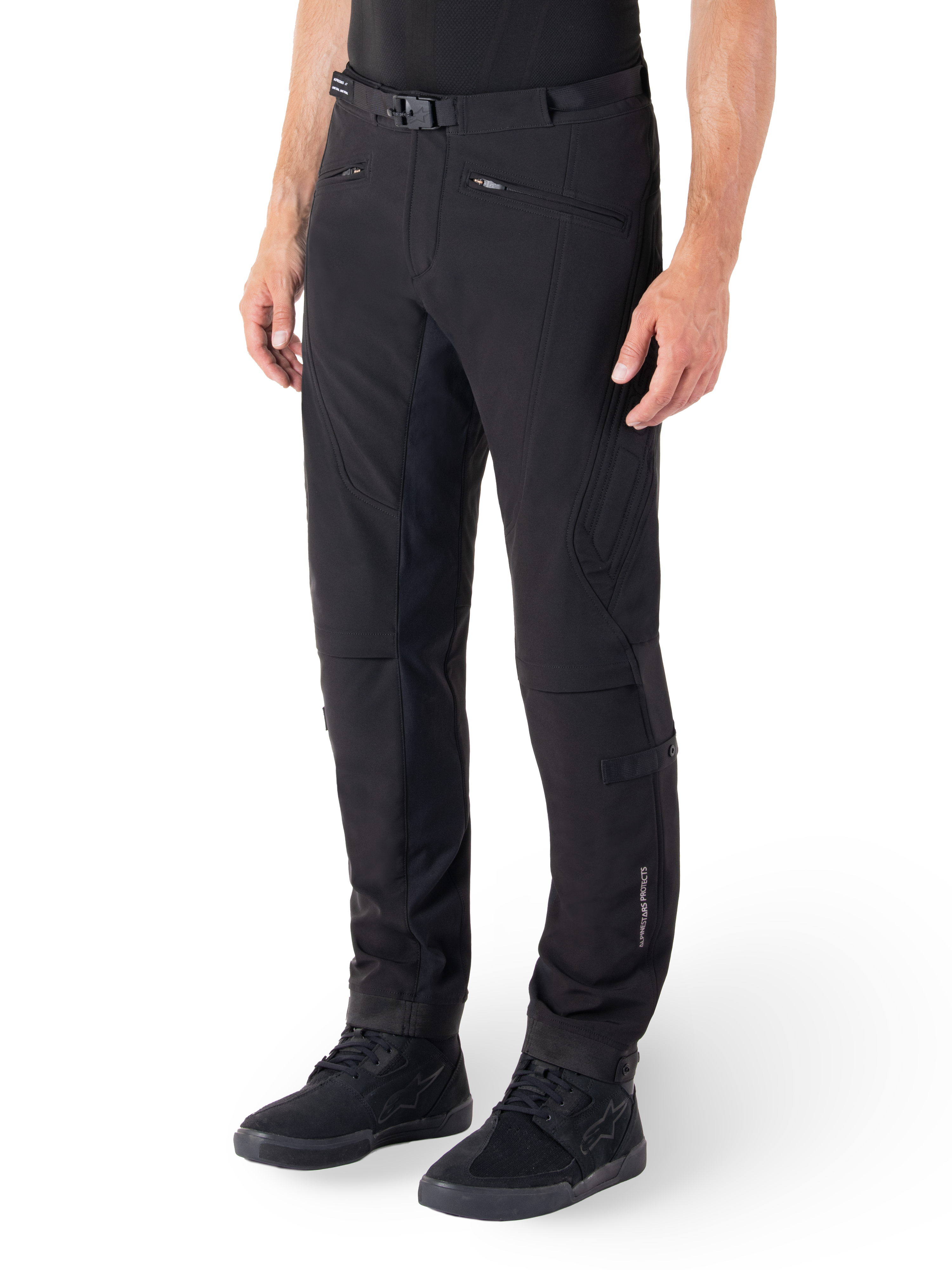 Pantaloni Alpinestars Alden, pantaloni da moto urban, nero, tessuto tecnico softshell con vestibilità regolare, caratterizzati da fibbia magnetica in vita, pannelli laterali trapuntati, tasche con zip e logo discreto sulla parte inferiore della gamba, indossati con scarpe da moto nere