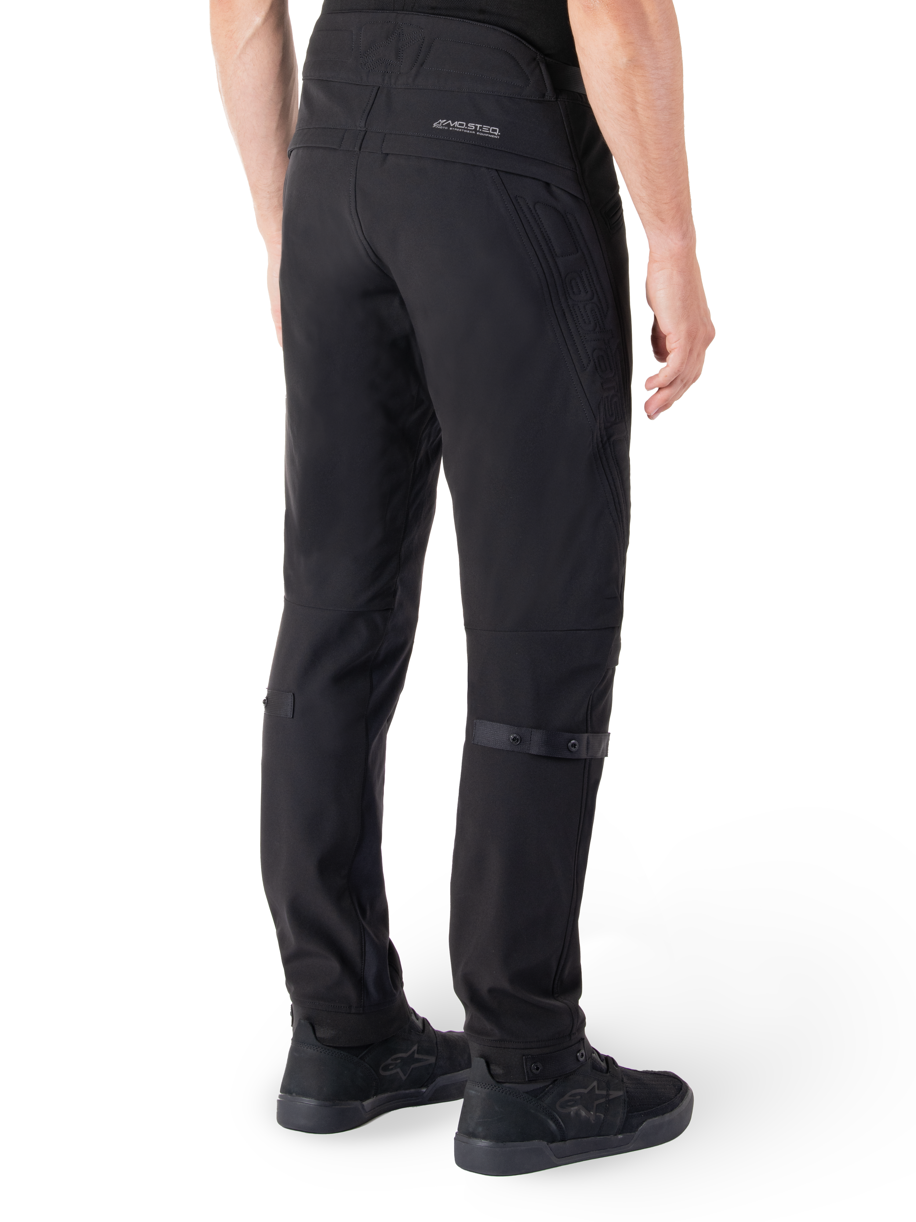 Alpinestars Alden Pants, pantaloni da moto urban, nero, vista posteriore che mostra il tessuto softshell tecnico con dettagli trapuntati, branding riflettente MO.ST.EQ. sul carré posteriore e cinturini regolabili sui polpacci, abbinati a scarpe da guida nere