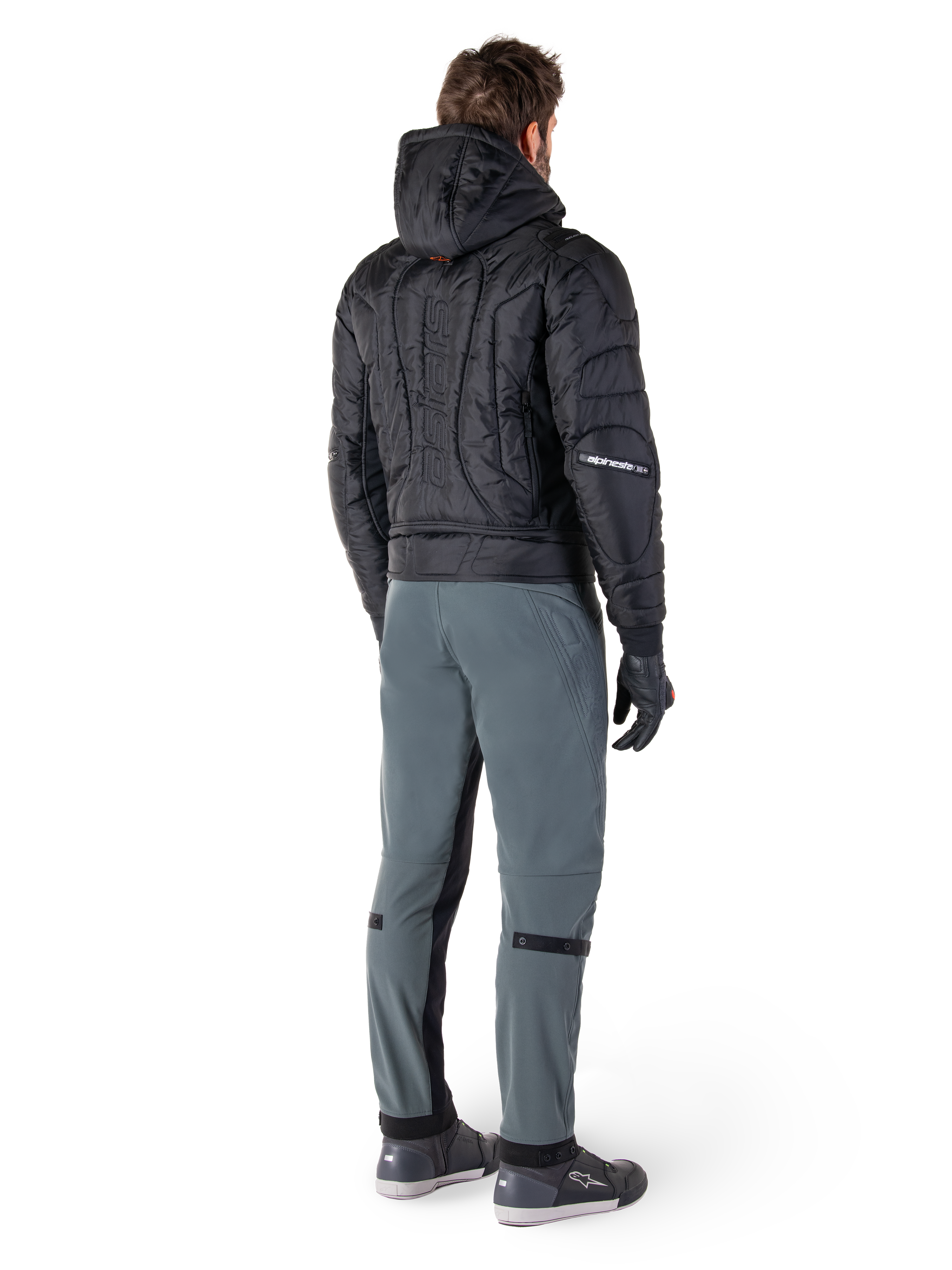 Pantaloni Alpinestars Alden, pantaloni da moto urban, Urban Gray, vista posteriore del motociclista che indossa una giacca nera trapuntata con cappuccio e scarpe da moto, vestibilità aderente sotto il ginocchio con pannelli elasticizzati neri e regolatori sulle ginocchia, design moderno ispirato allo streetwear.