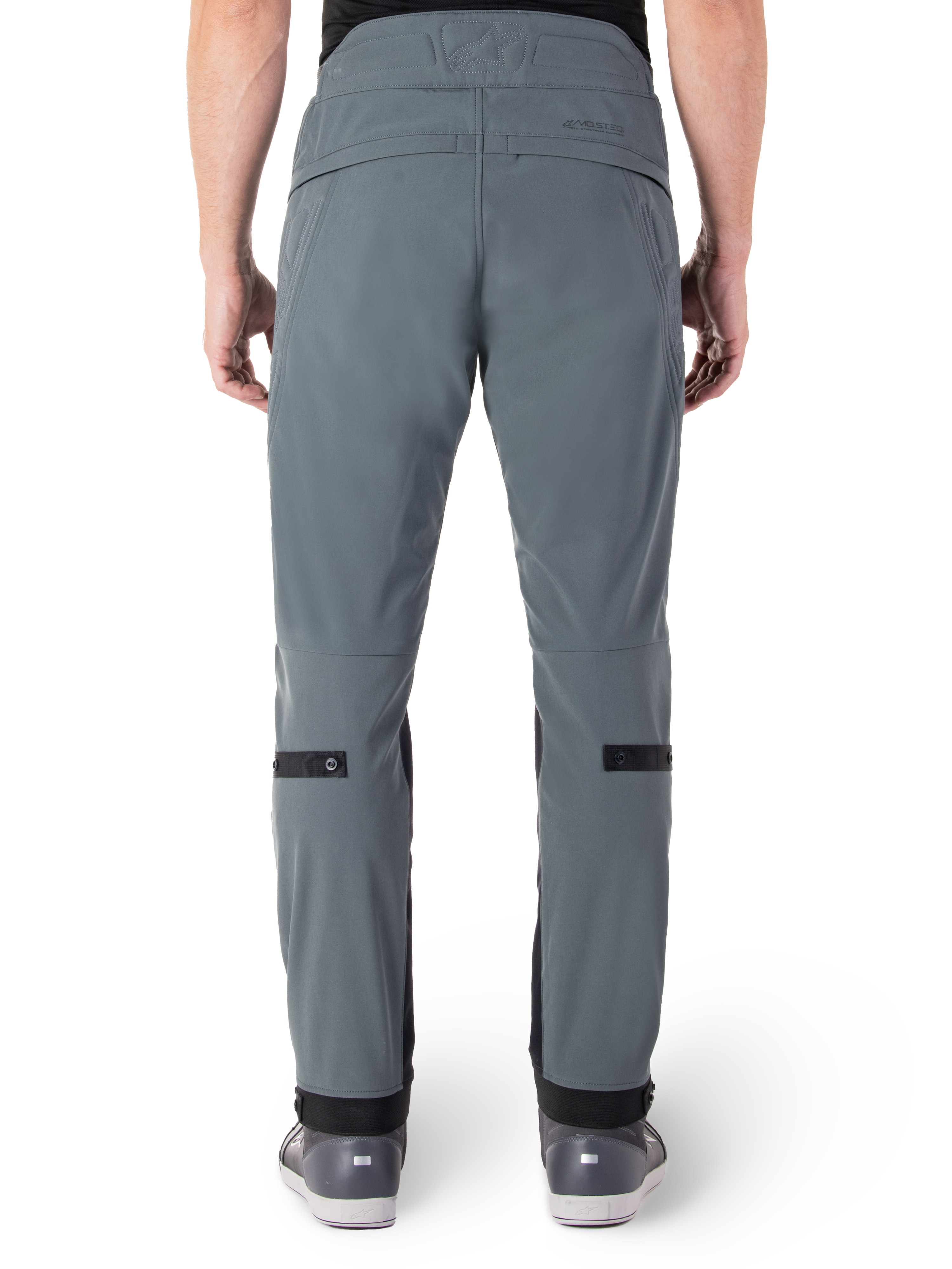Alpinestars Pantaloni Alden, Urban Gray, vista posteriore di pantaloni da moto urban da uomo, vestibilità aderente sotto il ginocchio con cinturini di regolazione neri sul polpaccio, design a vita alta con marchio MO.ST.EQ. sul carré posteriore, indossati con scarpe da moto grigie