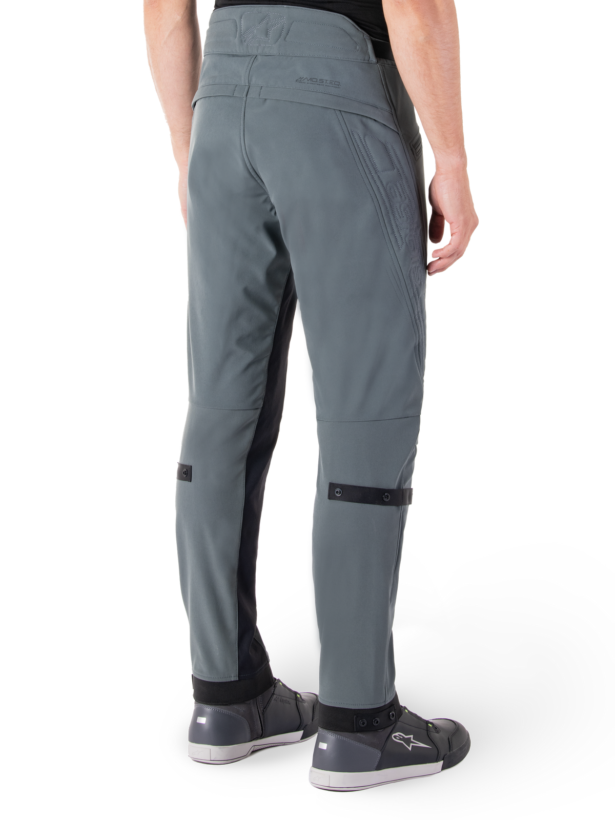 Pantaloni Alpinestars Alden, Urban Gray, vista posteriore laterale, pantaloni tecnici da moto ispirati allo streetwear con dettagli trapuntati sulla vita e cinturini neri sui polpacci, abbinati a scarpe da moto grigie, abbigliamento da moto urbano moderno
