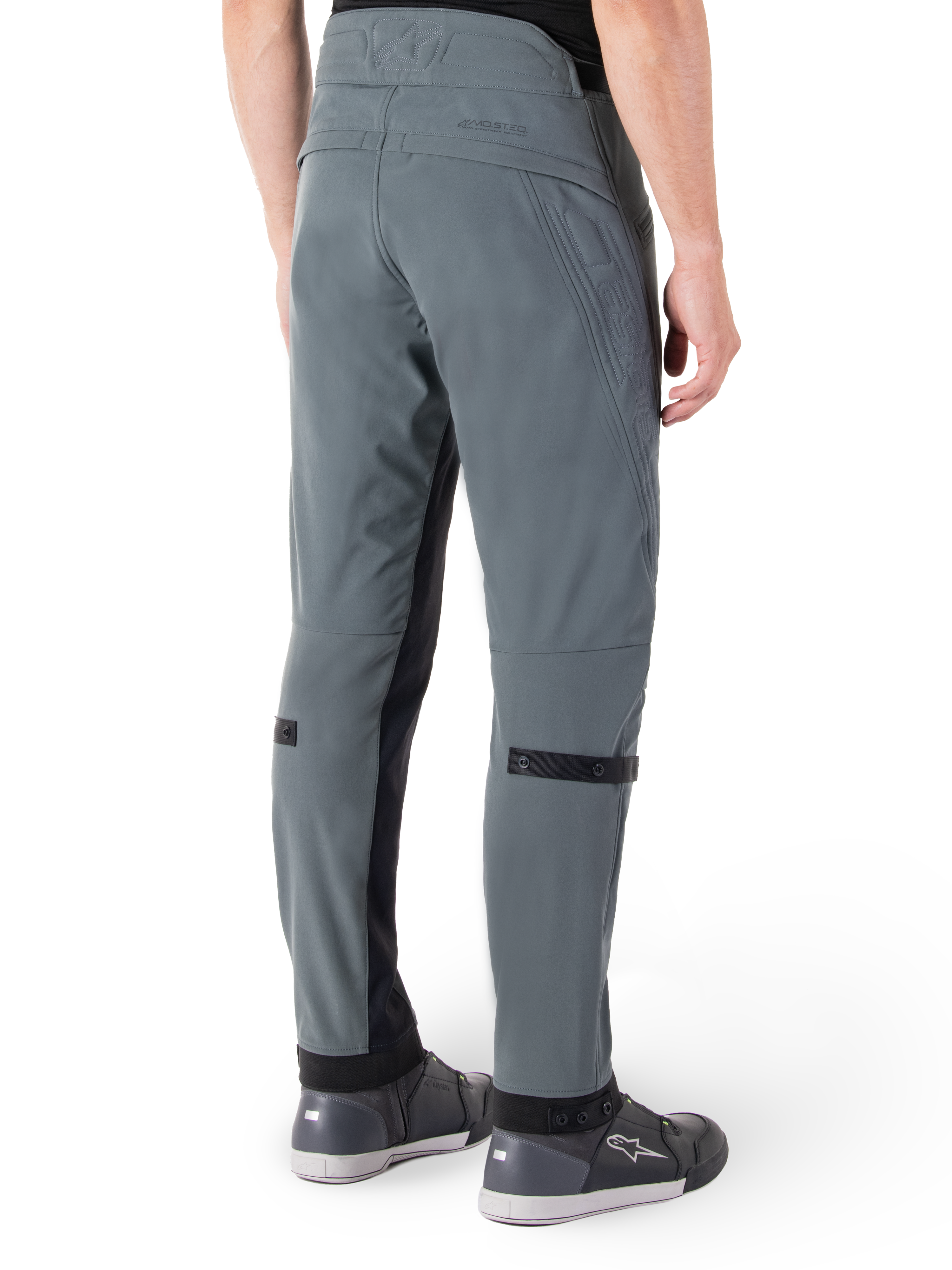 Pantaloni Alpinestars Alden, Urban Gray, vista posteriore laterale, pantaloni tecnici da moto ispirati allo streetwear con dettagli trapuntati sulla vita e cinturini neri sui polpacci, abbinati a scarpe da moto grigie, abbigliamento da moto urbano moderno