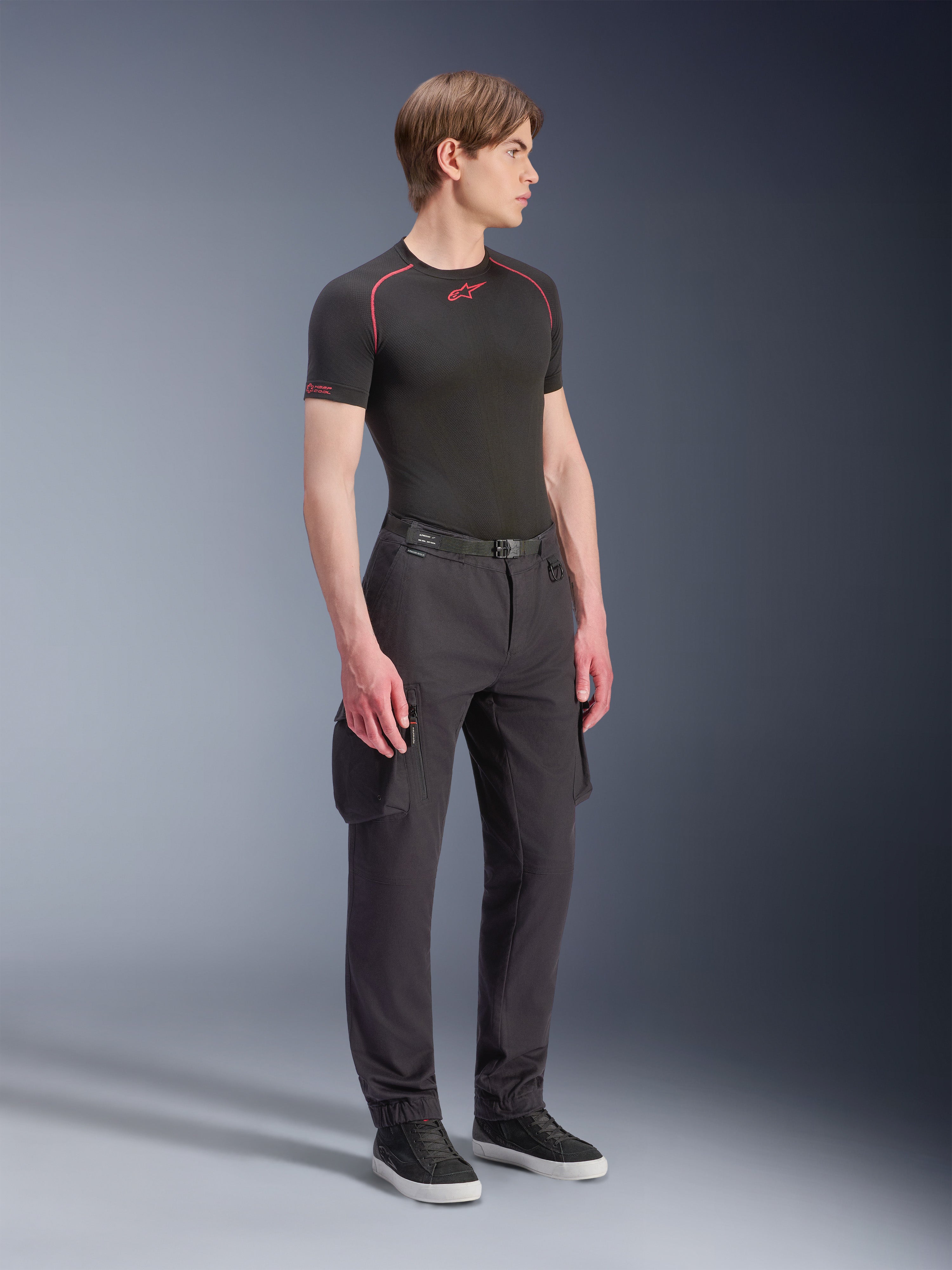 Modello che indossa i pantaloni Alpinestars Flex-AST Cargo - Short in nero, pantaloni cargo da moto urbani con tasche laterali e gambe affusolate, abbinati a un base layer nero e sneakers, abbigliamento da moto urbano.