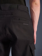 Alpinestars Flex-AST Cargo Pants, pantaloni da moto urban, nero, primo piano della parte posteriore e laterale che mostra la tasca posteriore con marchio Alpinestars, la patta della tasca cargo laterale e la robusta costruzione in tessuto elasticizzato.
