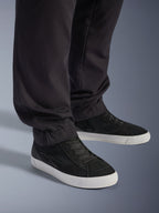 Alpinestars Flex-AST Cargo Pants, nero, pantaloni da moto urban, vista ravvicinata delle gambe affusolate e degli orli elasticizzati, abbinati a sneakers bianche e nere, tessuto tecnico in twill di policotone per la guida su strada casual